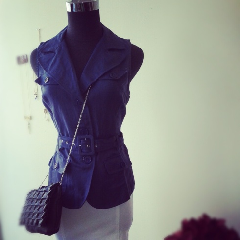 Slate blue sleeveless trench blouse with grey crossover clutch and white double-seam skirt.